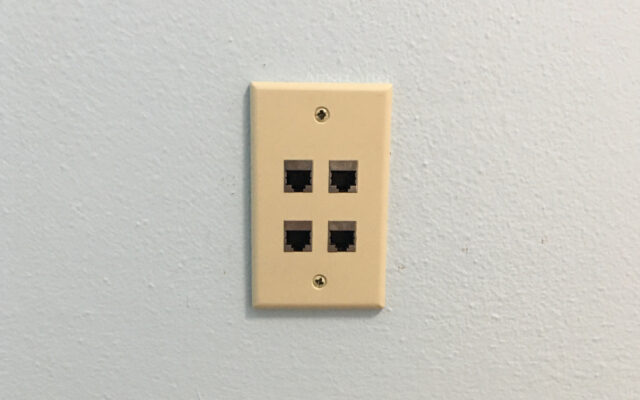 A photo of a pale blue wall with a beige four-port Ethernet wall plate at the center.